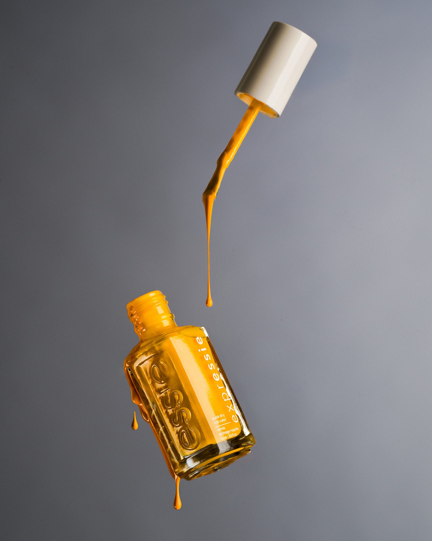 Floating bottle of Essie Expressie yellow nail polish with brush suspended mid-drip. Captured by Toronto-based commercial photographer Nicholas Hyatt, specializing in dynamic product still life.