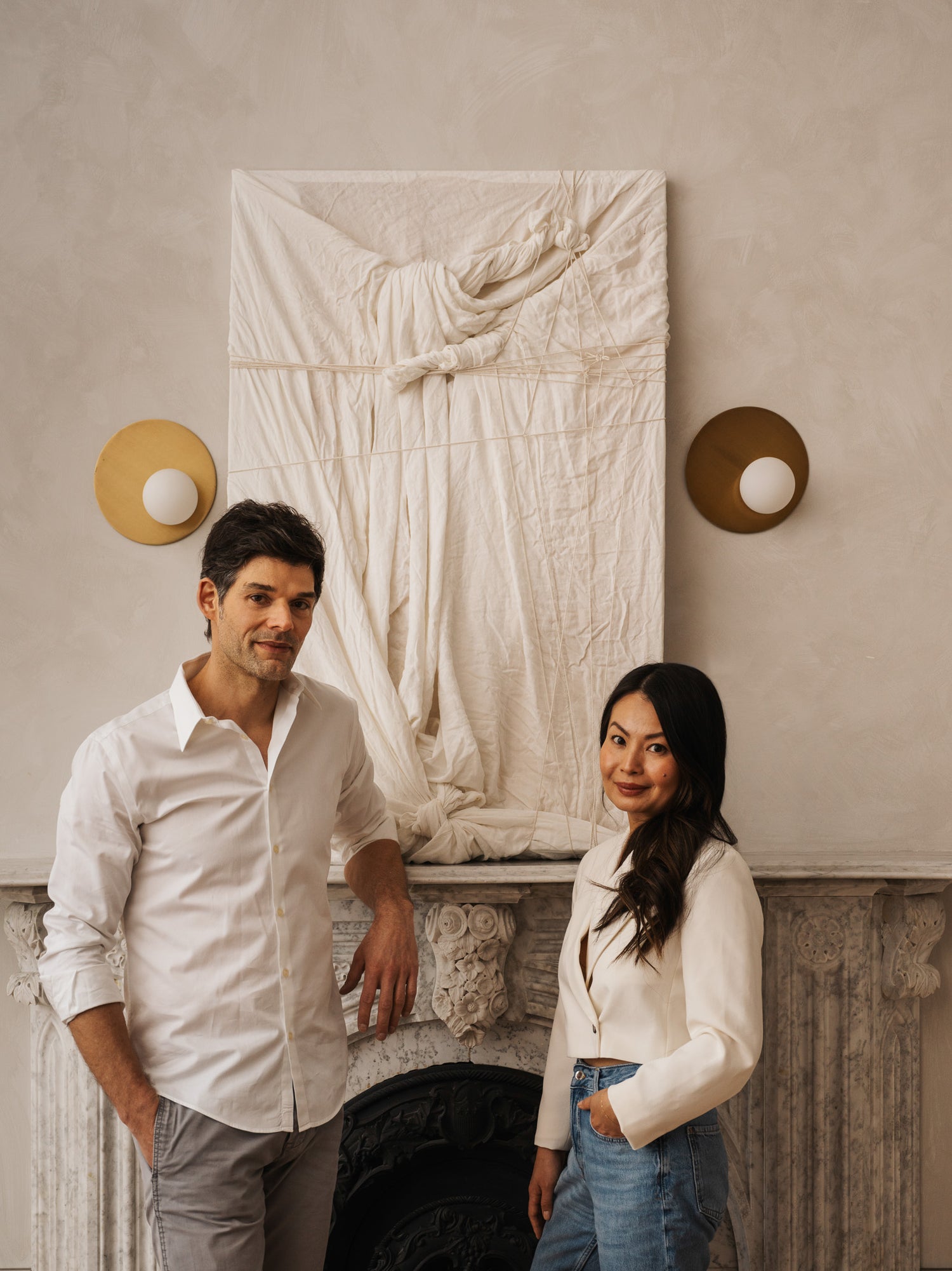 Portrait of Lune 1860 founders Lisa Mok and Ezra Silverton standing in front of a marble fireplace and sculptural wall hanging inside their Goderich venue — elegant editorial image by photographer Nicholas Hyatt.
