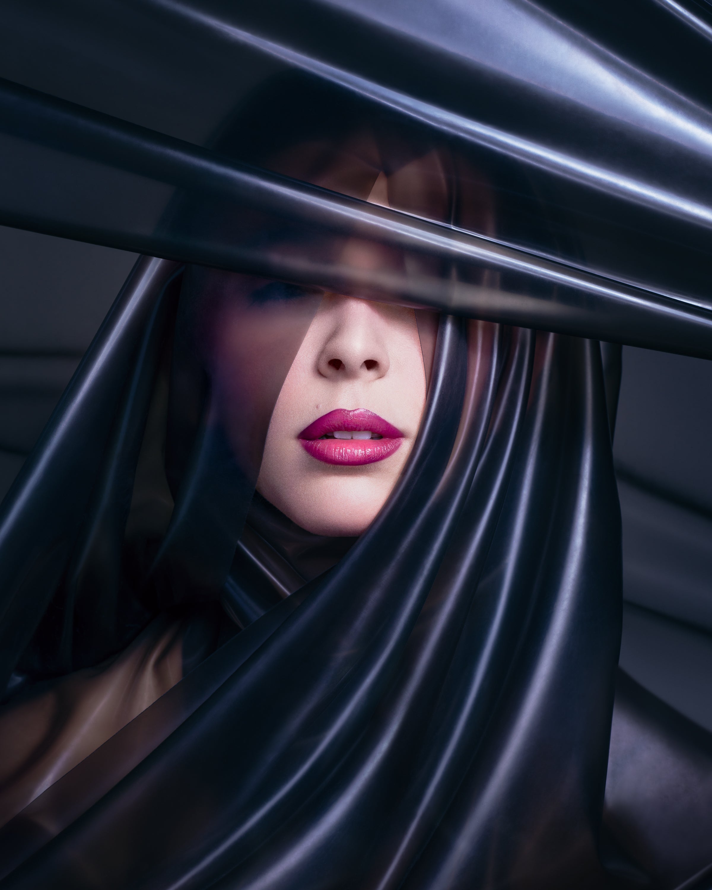 A mysterious close-up beauty portrait of a woman with glossy magenta lips, partially veiled by layers of sheer black plastic. Captured by Toronto-based photographer Nicholas Hyatt, blending sensuality with conceptual beauty photography.