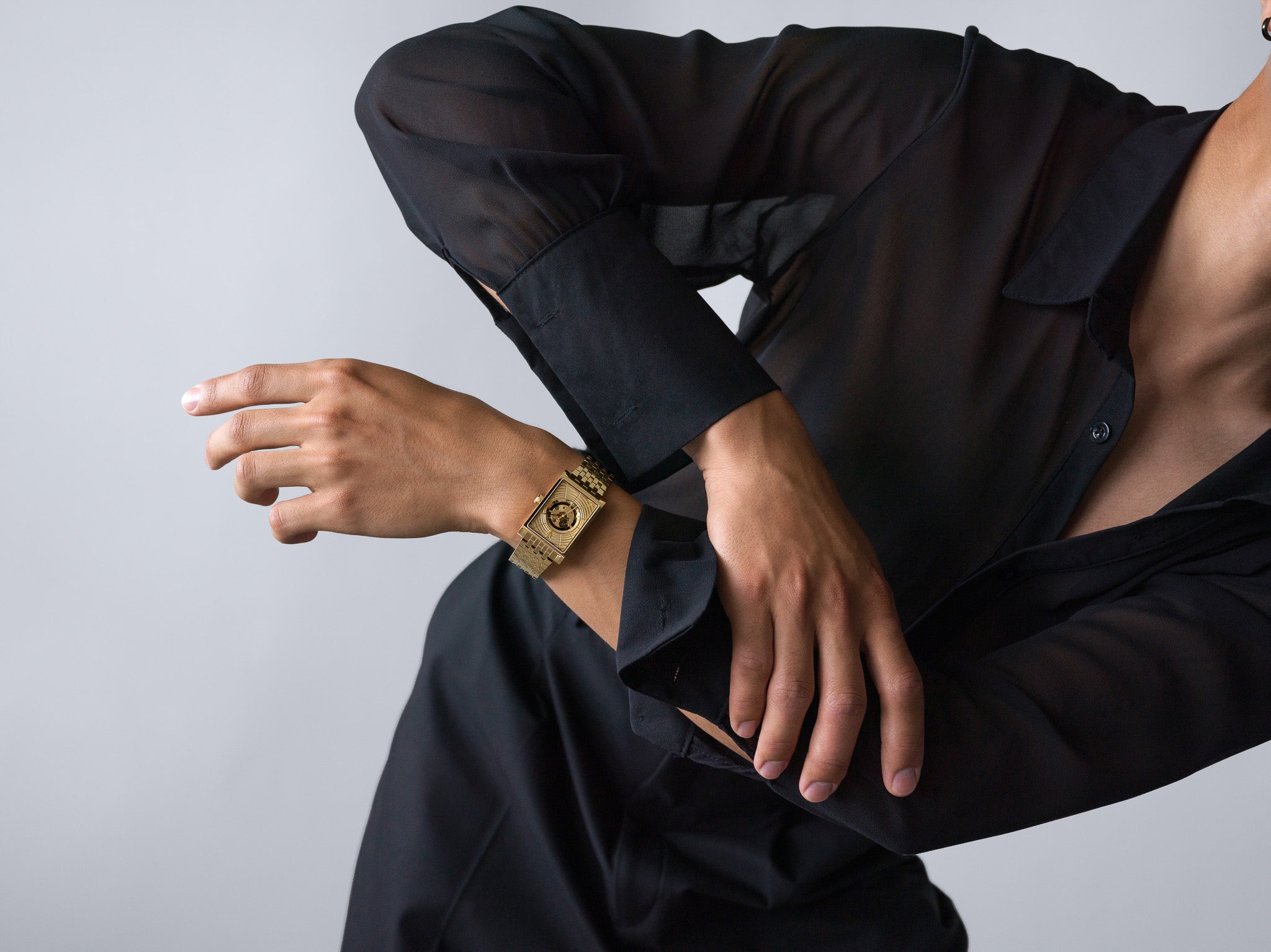 A close-cropped portrait of a model dressed in a sheer black shirt, striking a dynamic pose with a gold Vieren watch on their wrist. The watch’s rectangular face and mechanical details reflect luxury and craftsmanship. Photographed by Toronto-based commercial photographer Nicholas Hyatt, this image fuses fashion editorial energy with high-end product focus.