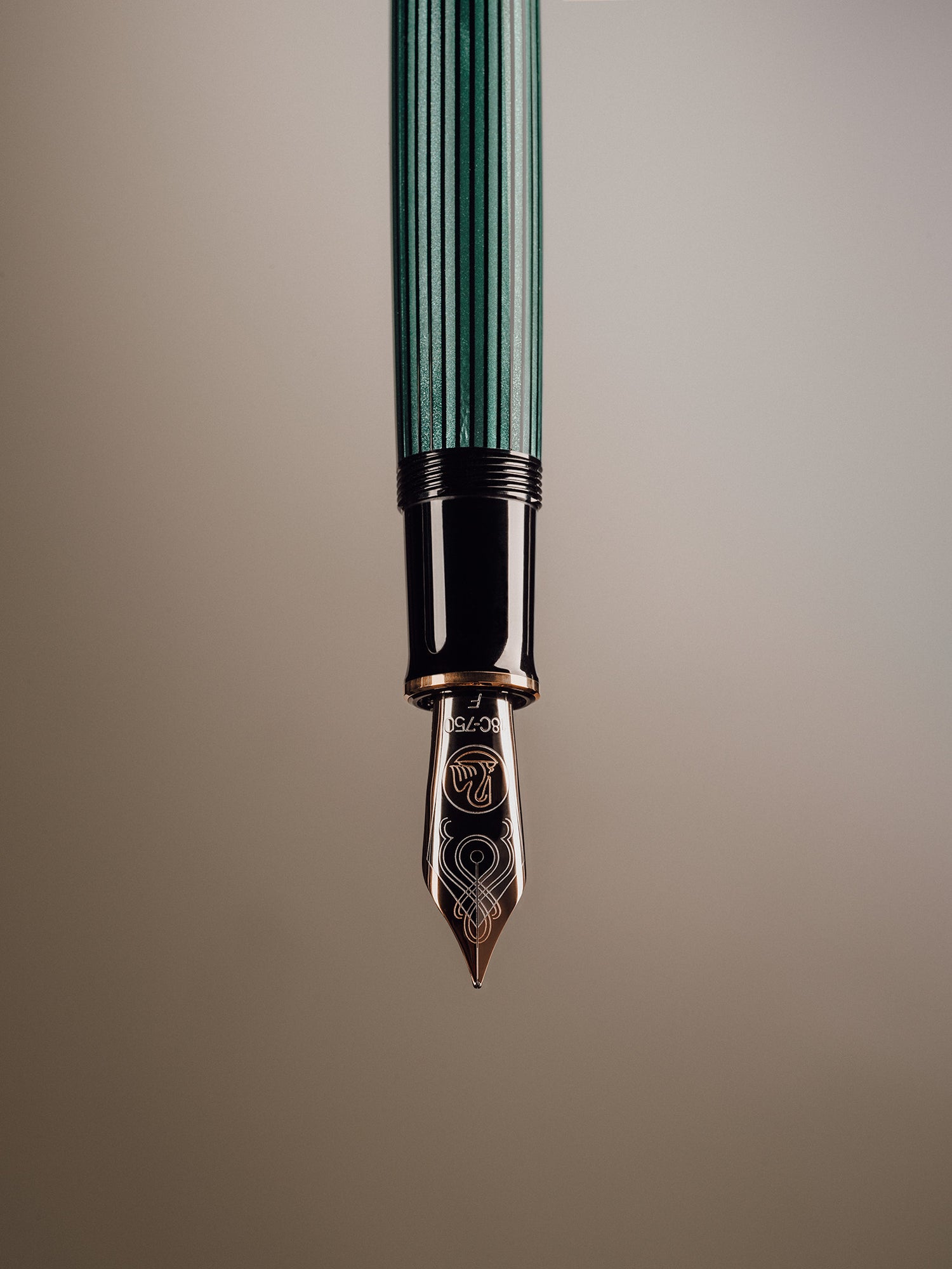 An editorial close-up of a luxury Pelikan M1000 fountain pen suspended vertically, with a focus on the engraved gold nib and glossy black and green barrel. Photographed by Toronto-based product photographer Nicholas Hyatt, the image highlights fine craftsmanship and design in premium writing instruments.