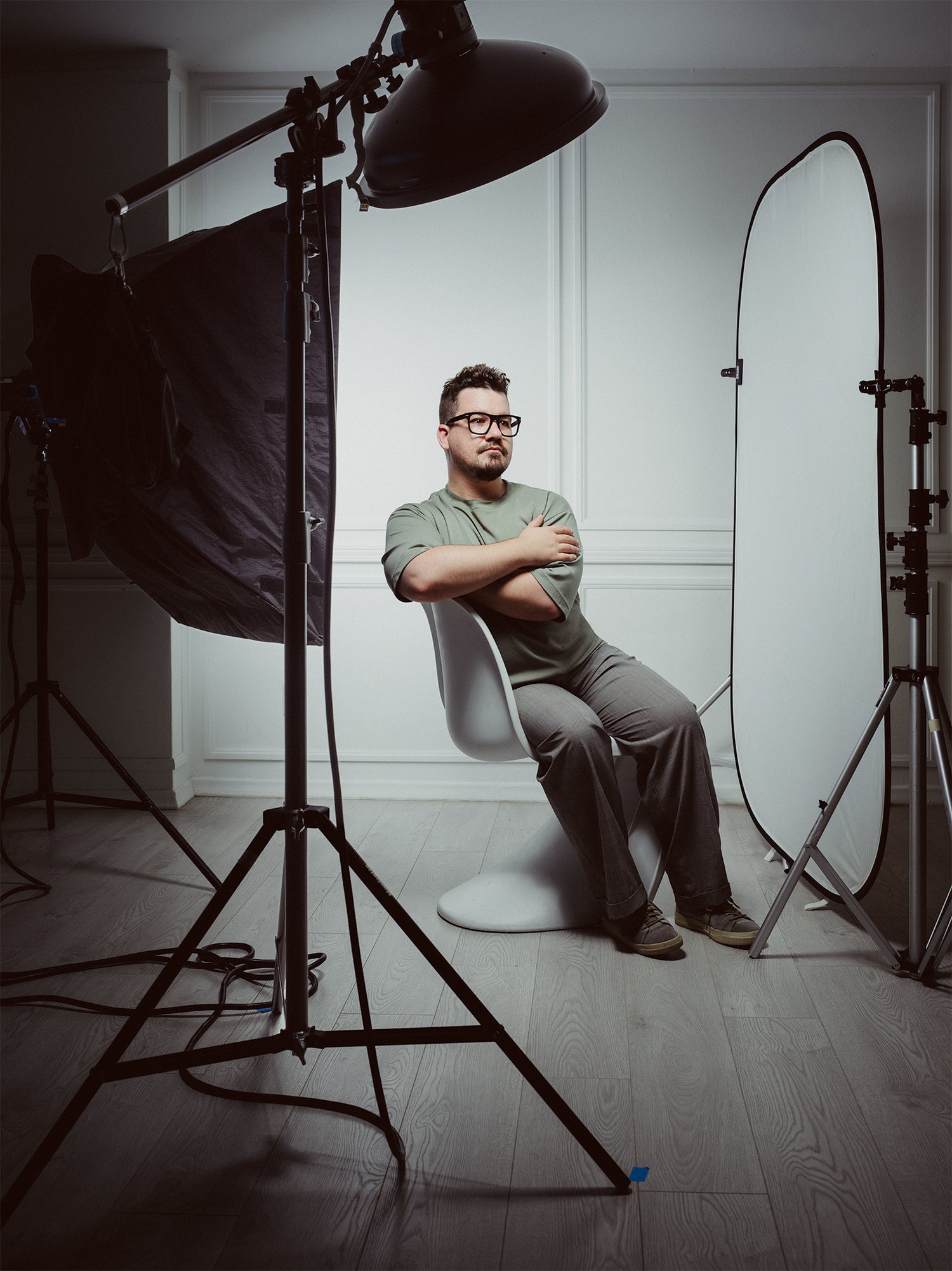 Studio portrait of Toronto-based commercial and editorial photographer Nicholas Hyatt seated under professional lighting equipment, captured in a minimalist white-walled photography studio. The image highlights behind-the-scenes of a creative workspace and personal branding for artists.