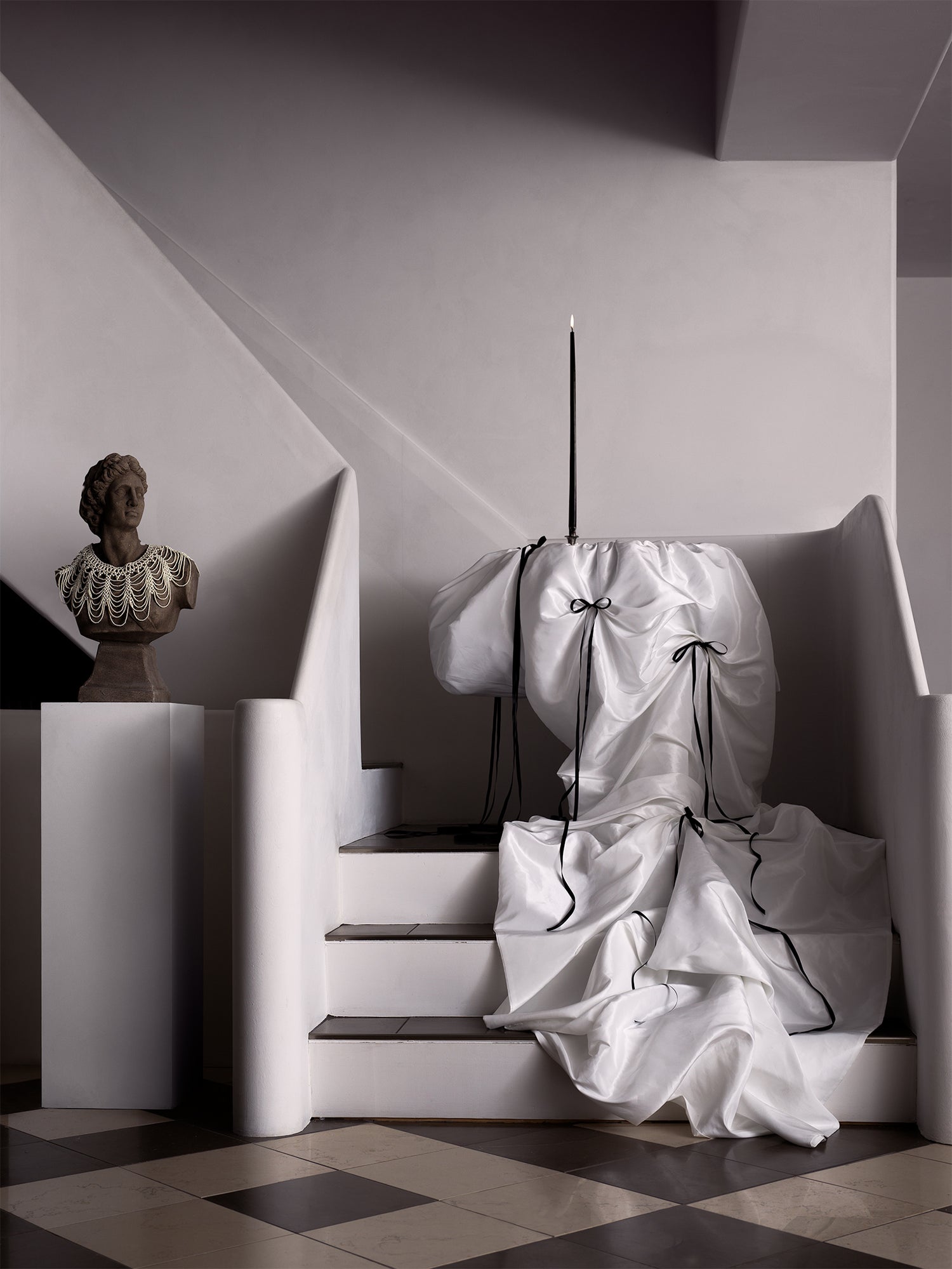  dramatic interior still life features a black taper candle on a satin-draped pedestal, a classical bust adorned with pearls, and bold architectural lines. Captured by Toronto-based photographer Nicholas Hyatt at LUNE 1860, Goderich, the image evokes baroque opulence with a modern, sculptural twist.